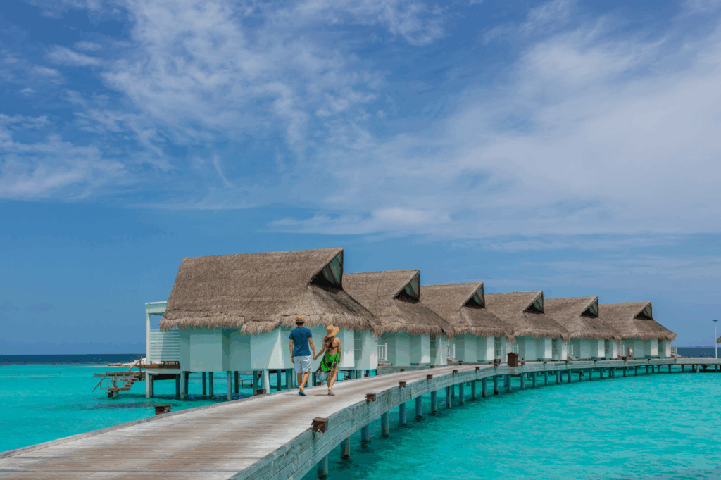 Couple walking along boardwalk to overwater villas, Machchafushi Island Resort & Spa, Maldives