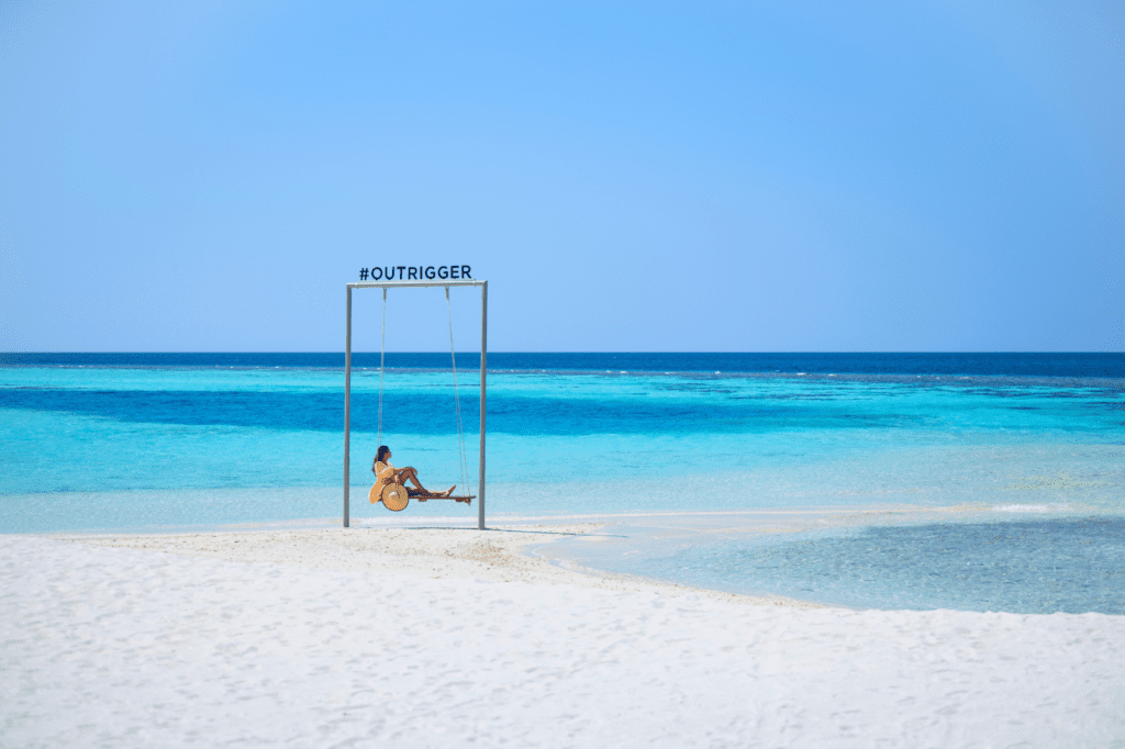 Woman on beach swing at Outrigger Maldives Maafushivaru