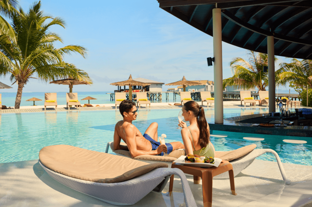 A couple enjoying a drink pool-side on loungers at Centara Ras Fushi Resort & Spa, Maldives